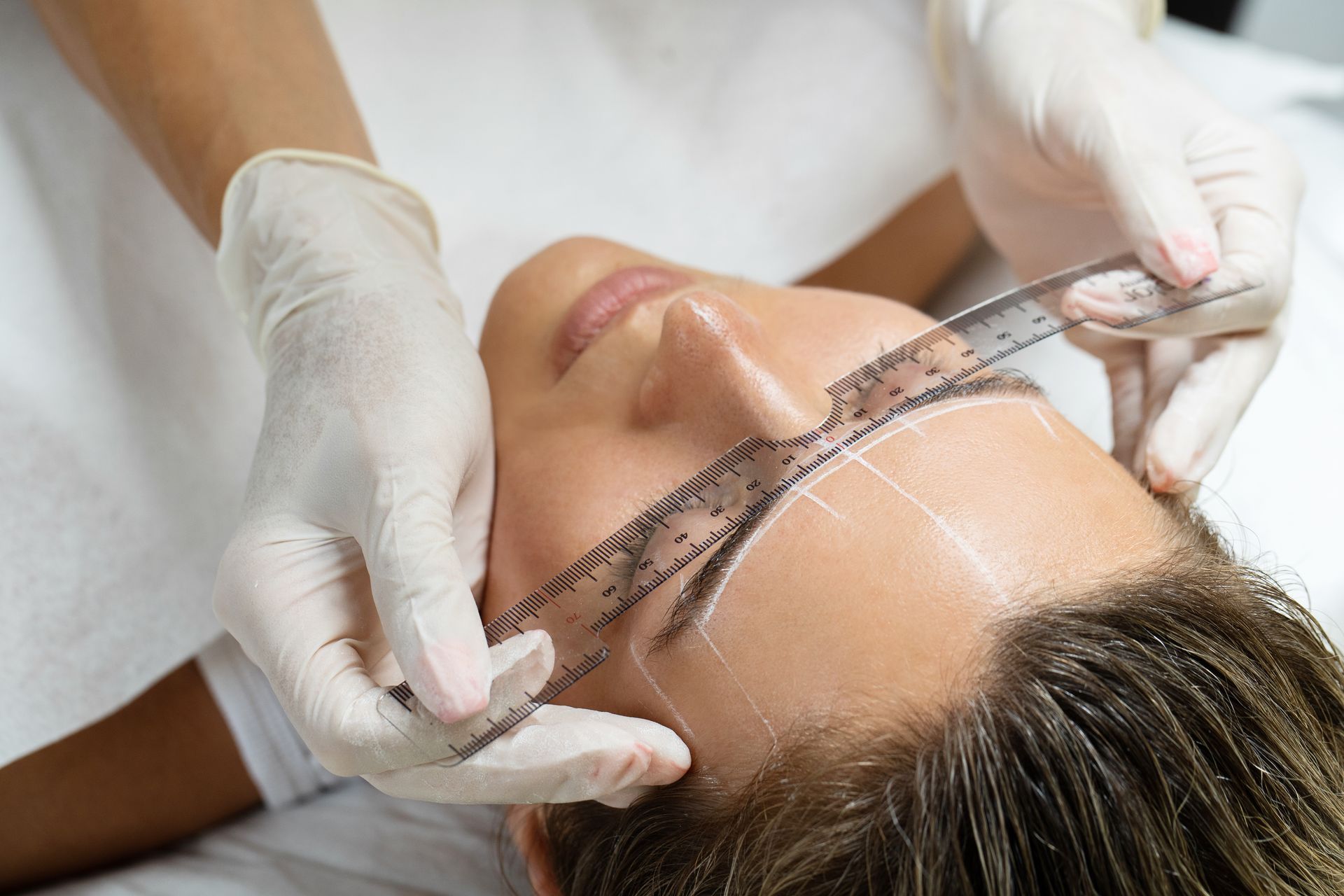 A woman is measuring her eyebrows with a ruler.