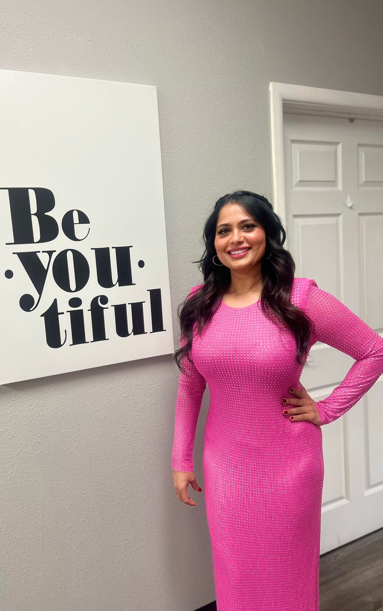 A woman in a pink dress is standing in front of a sign that says `` be youtiful ''.