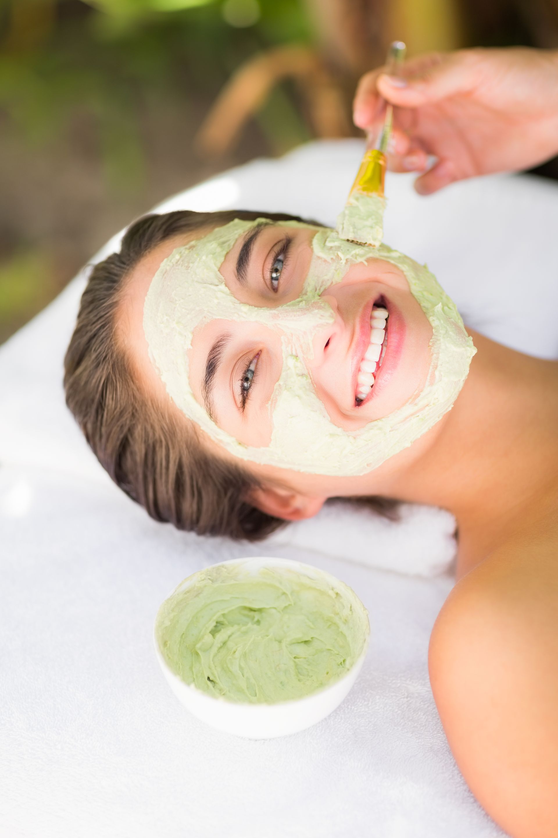 A woman is getting a green face mask at a spa.