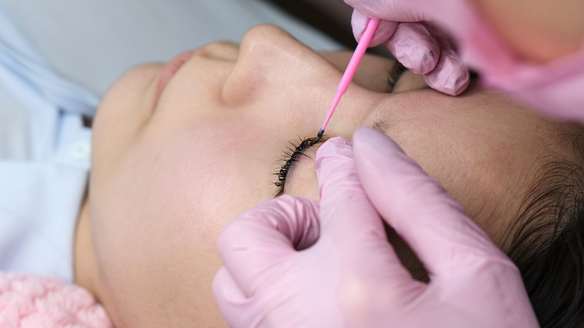 A woman is getting her eyebrows done by a woman wearing pink gloves.