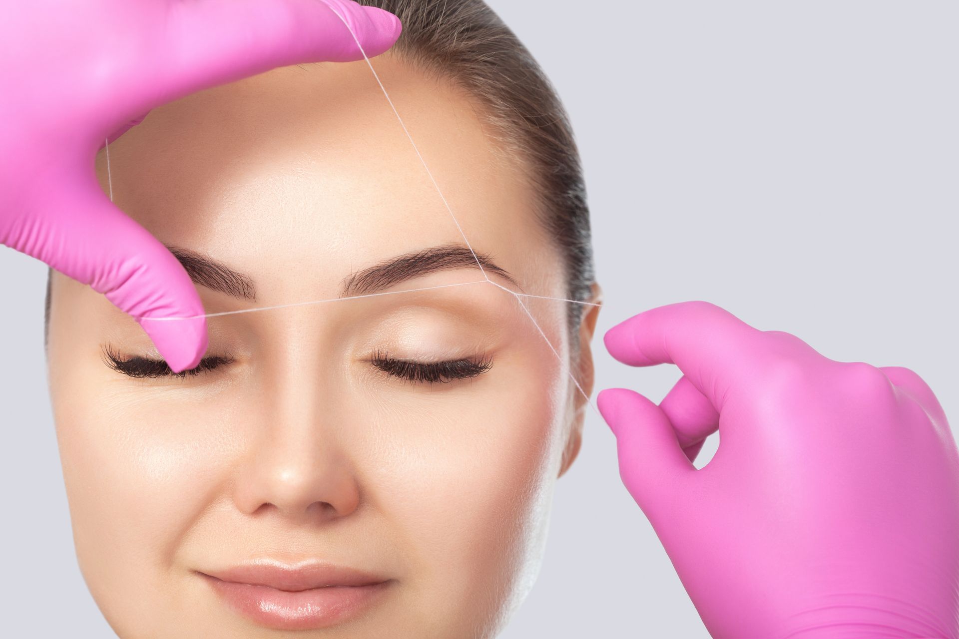 A woman is getting her eyebrows threaded with pink gloves.