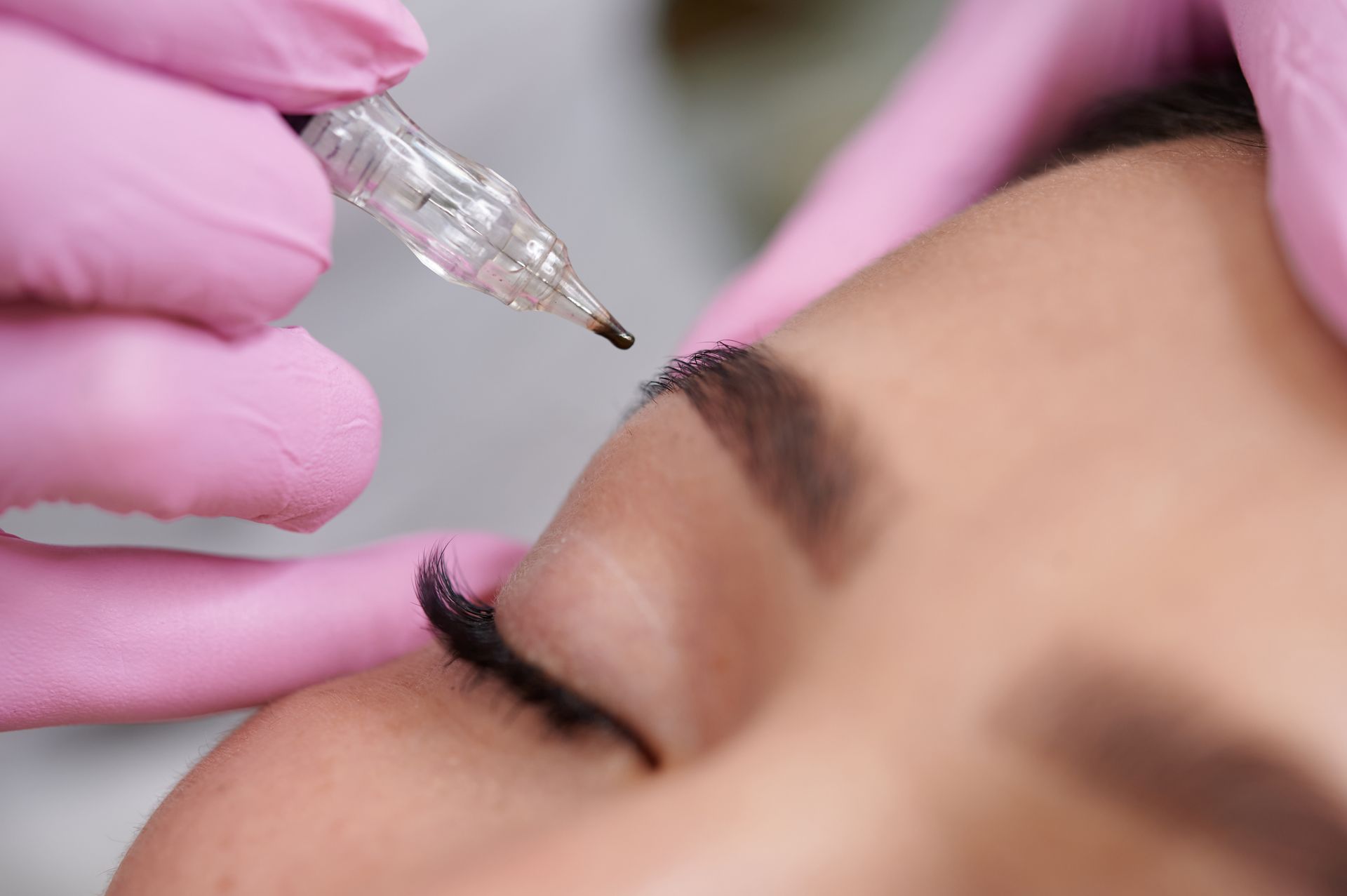 A woman is getting a permanent makeup tattoo on her eyebrows.