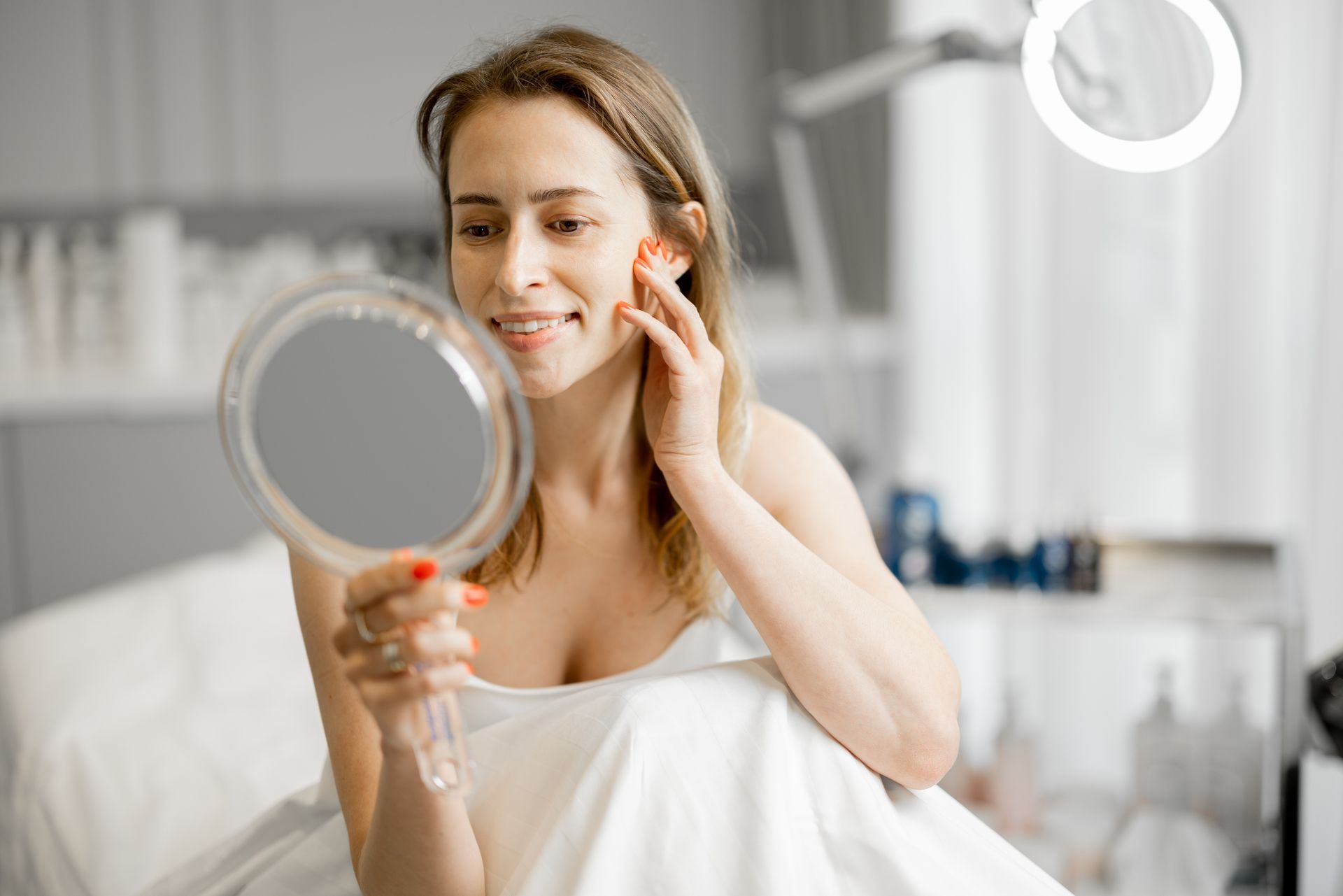 A woman is sitting on a bed looking at her face in a mirror.