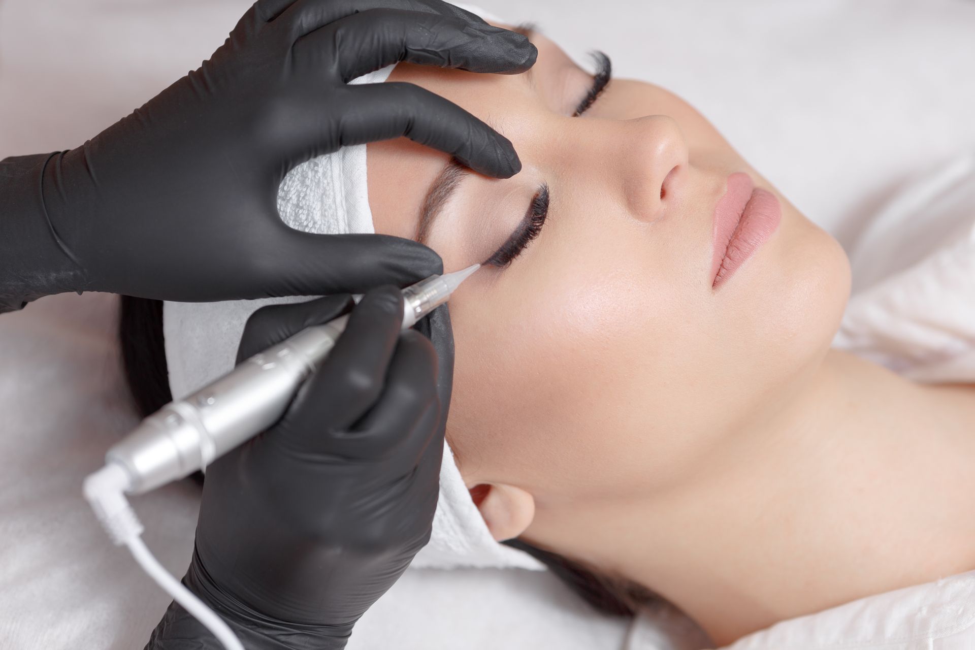 A woman is getting a permanent makeup treatment on her eyebrows.