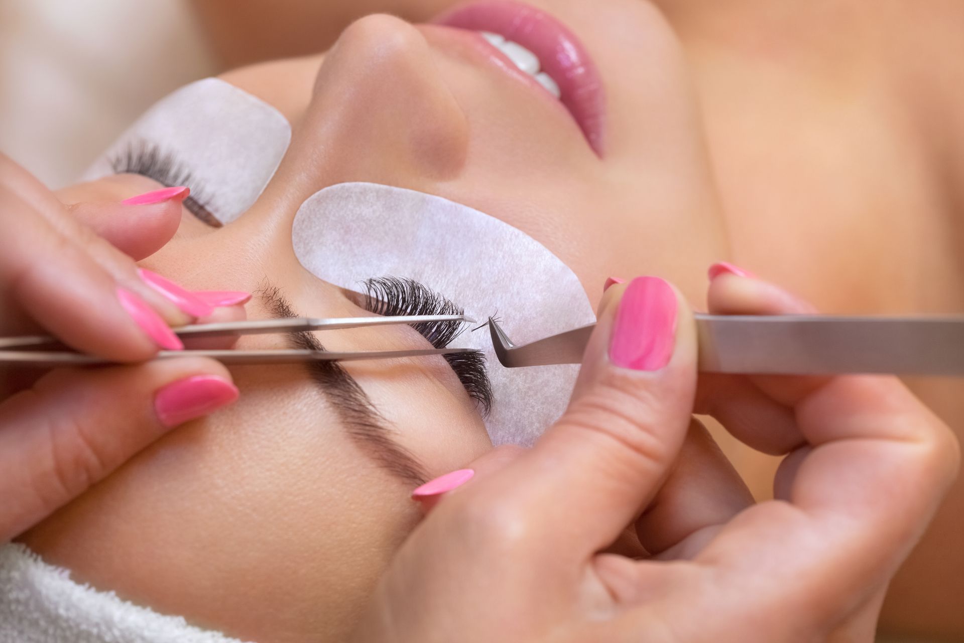 A woman with pink nails is getting eyelash extensions.