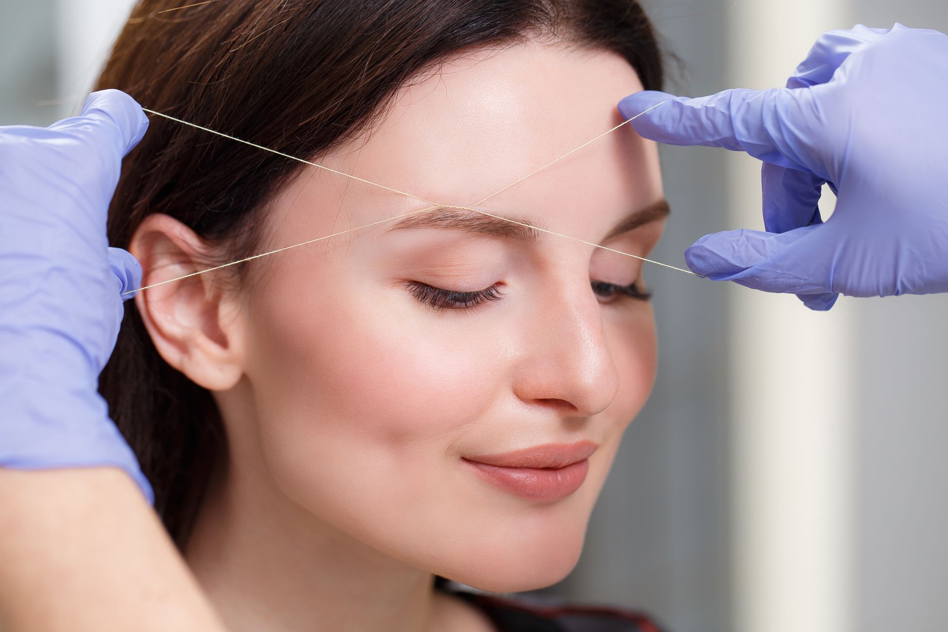 A woman is getting her eyebrows threaded by a doctor.