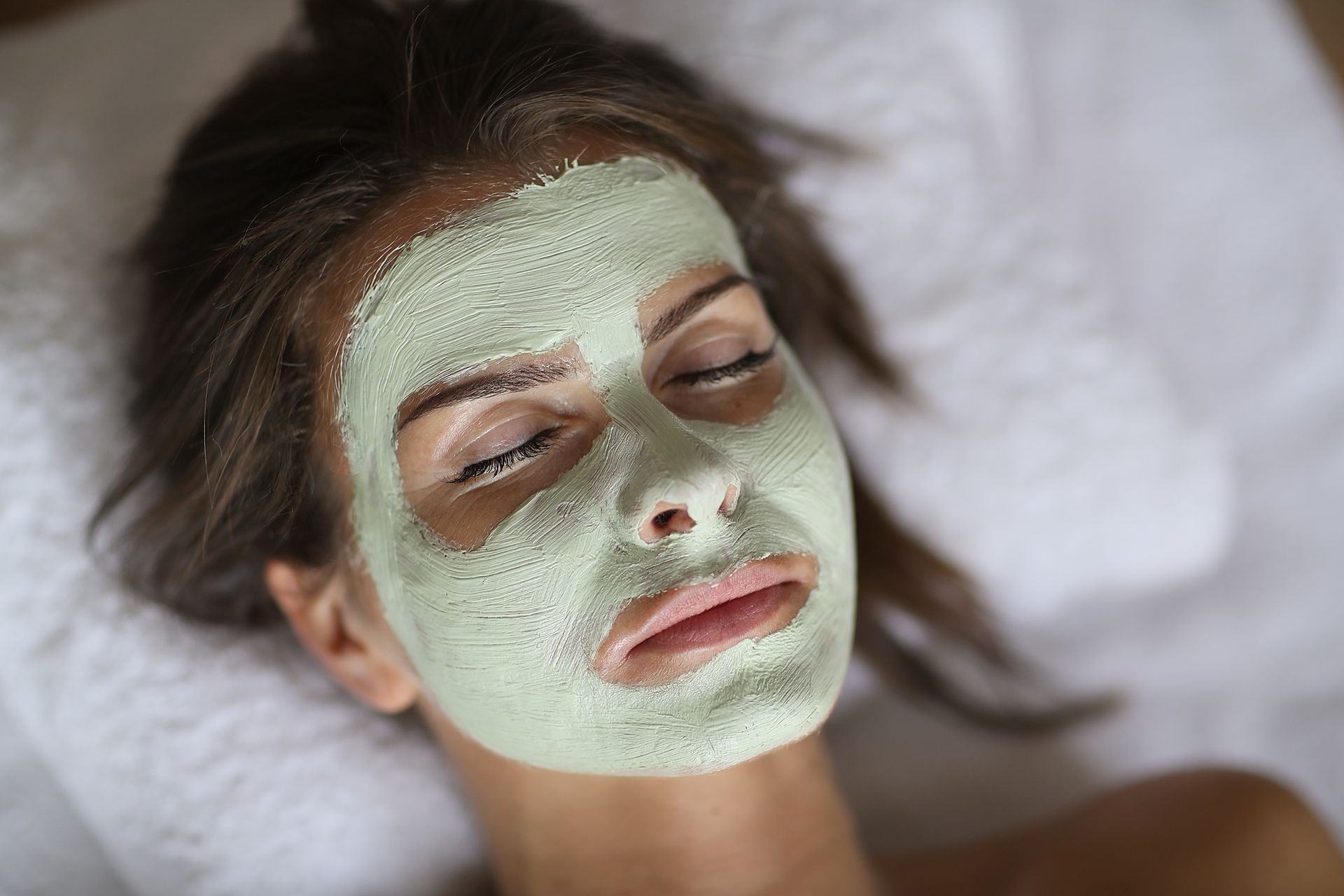 A woman is laying on a bed with a green mask on her face.