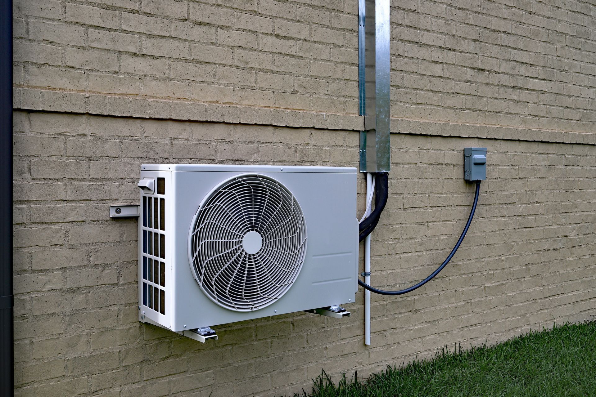Outdoor air conditioning condenser unit mounted on a brick wall with an electrical conduit.