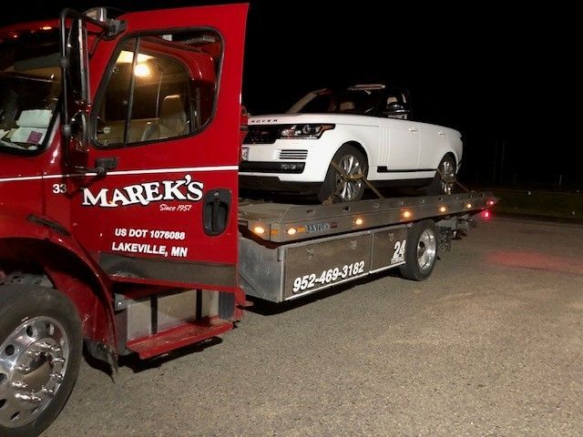 A yellow tow truck is carrying a car on a highway.