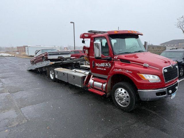 Red tow truck with a car on the flatbed in a snowy parking lot.