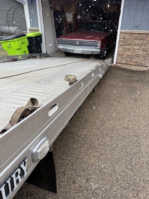 A burgundy car being loaded onto a tow truck ramp in a driveway.