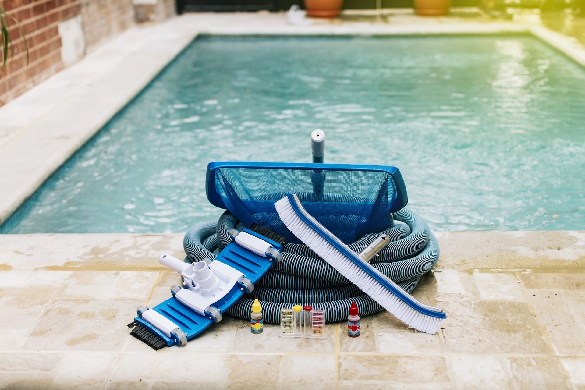 Pool cleaning supplies on pool deck: net, hose, vacuum, brush, and chemical test kit.