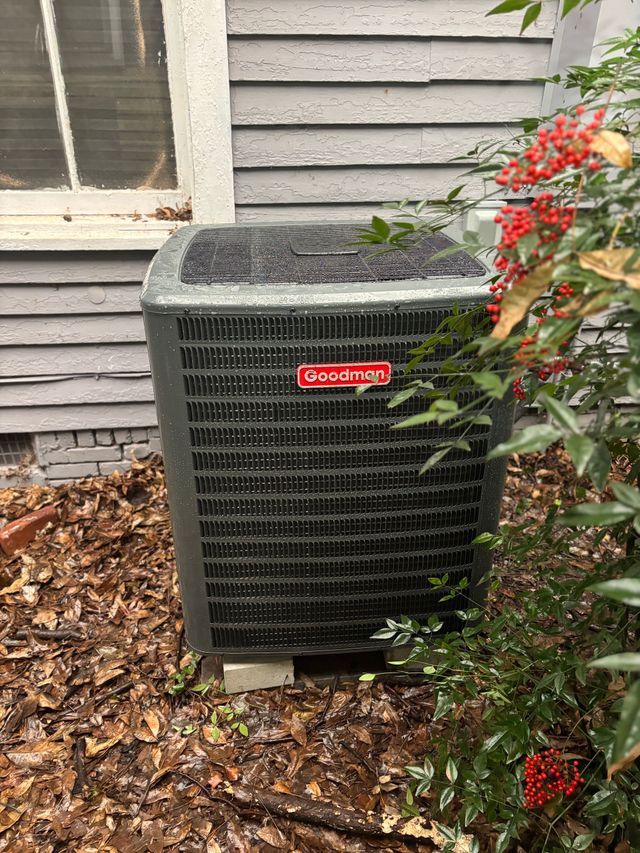 Outdoor air conditioner beside a house, with leaves on top and red flowers in the foreground