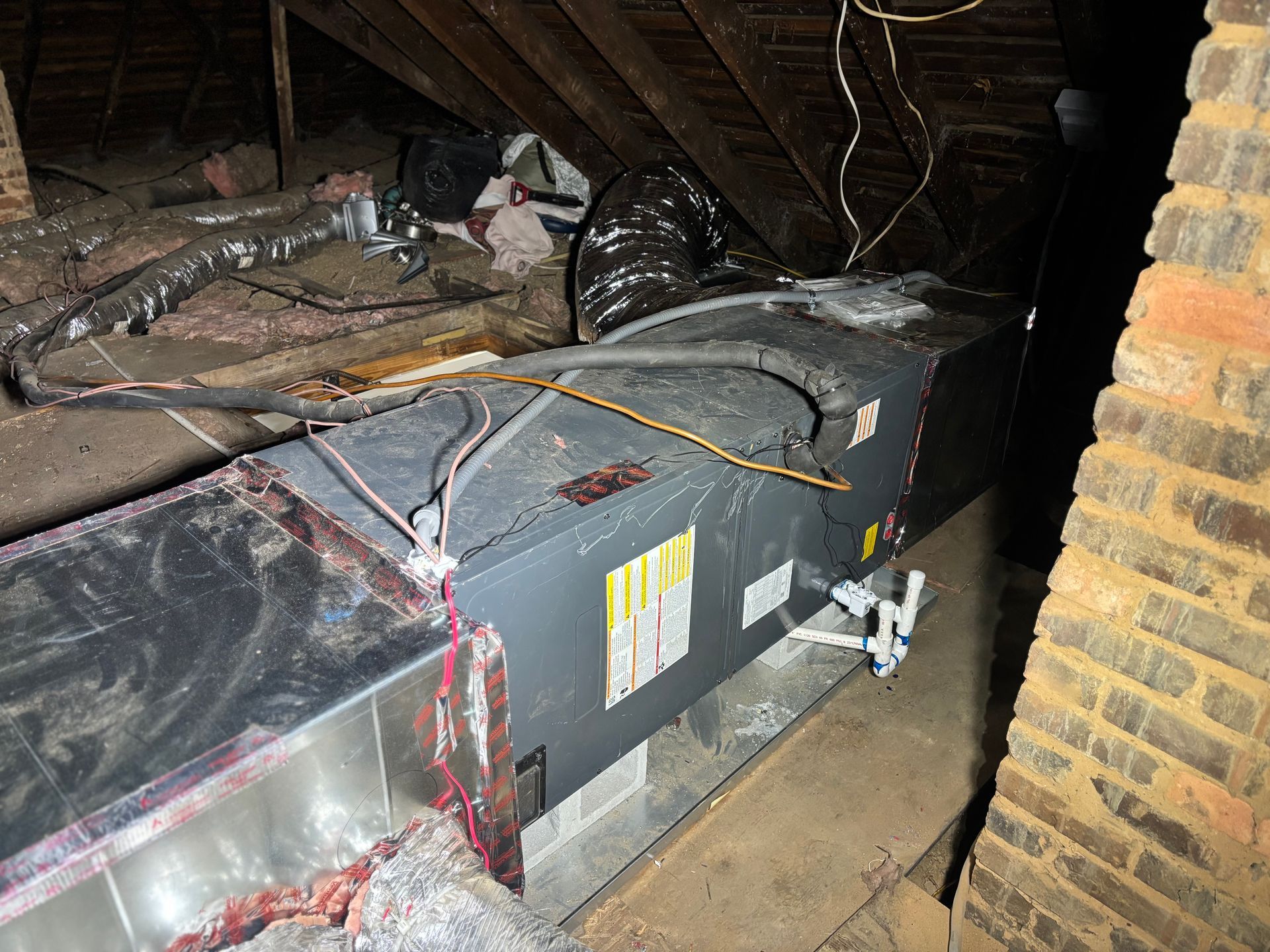 Attic HVAC unit with exposed ductwork and wiring beneath a sloped roof.