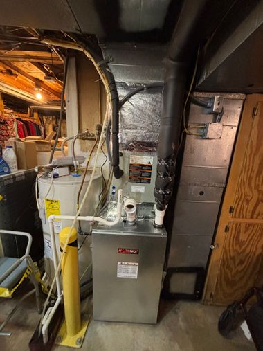 Basement furnace and ductwork beside a water heater, with exposed insulation and pipes.