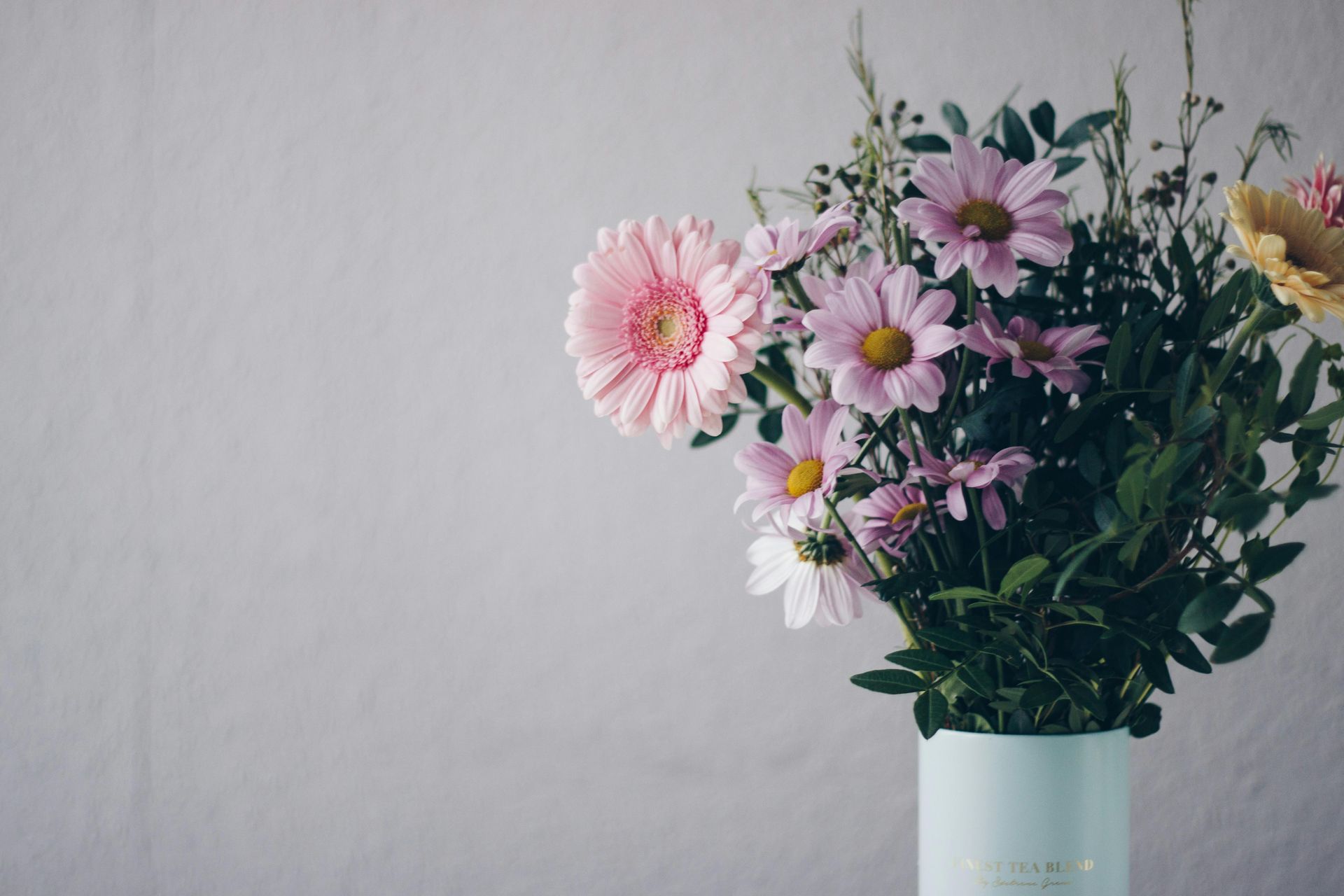 Bouquet of pink and purple flowers in a light blue vase against a gray wall.
