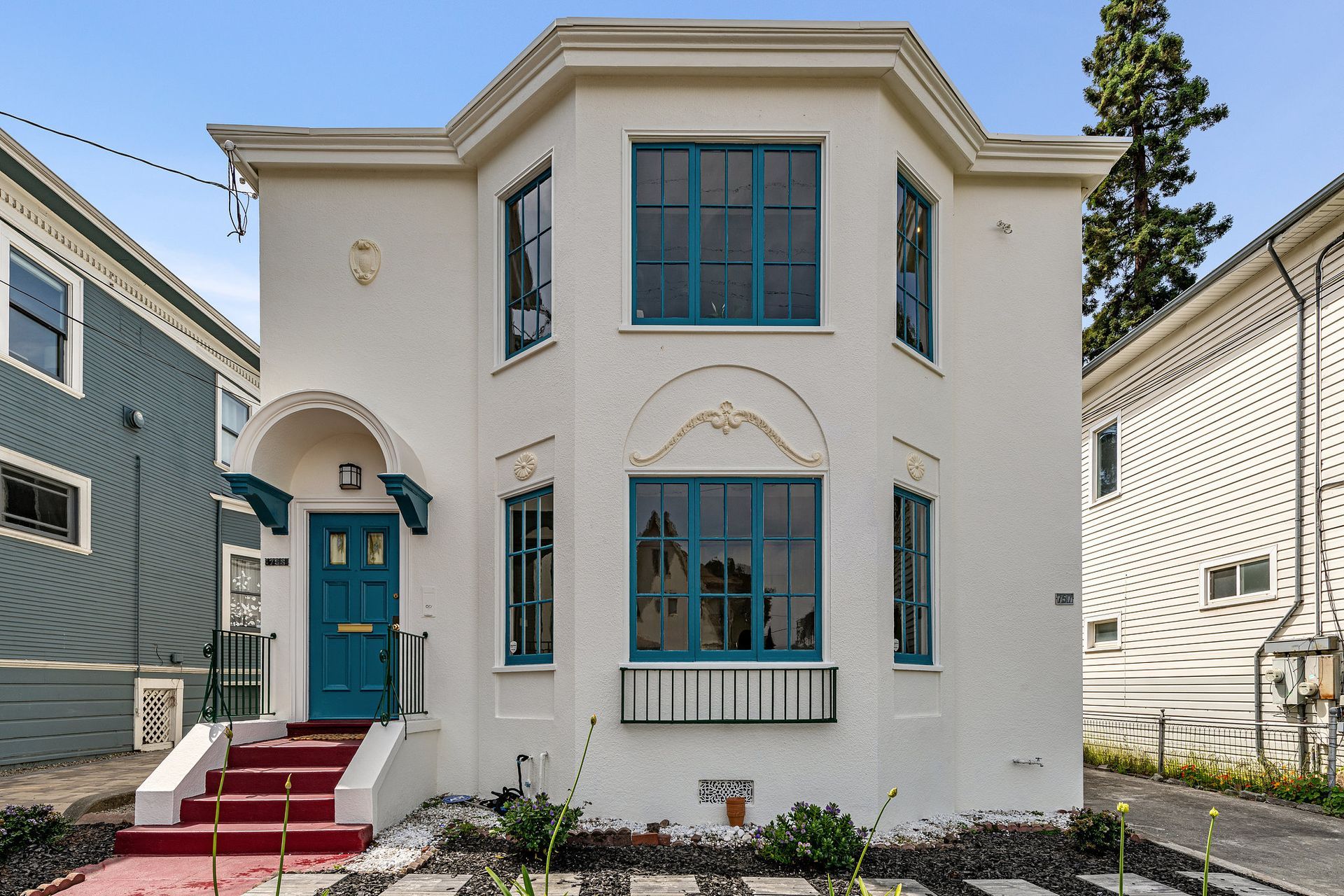 White house with turquoise windows and door, red stairs, and black accents.