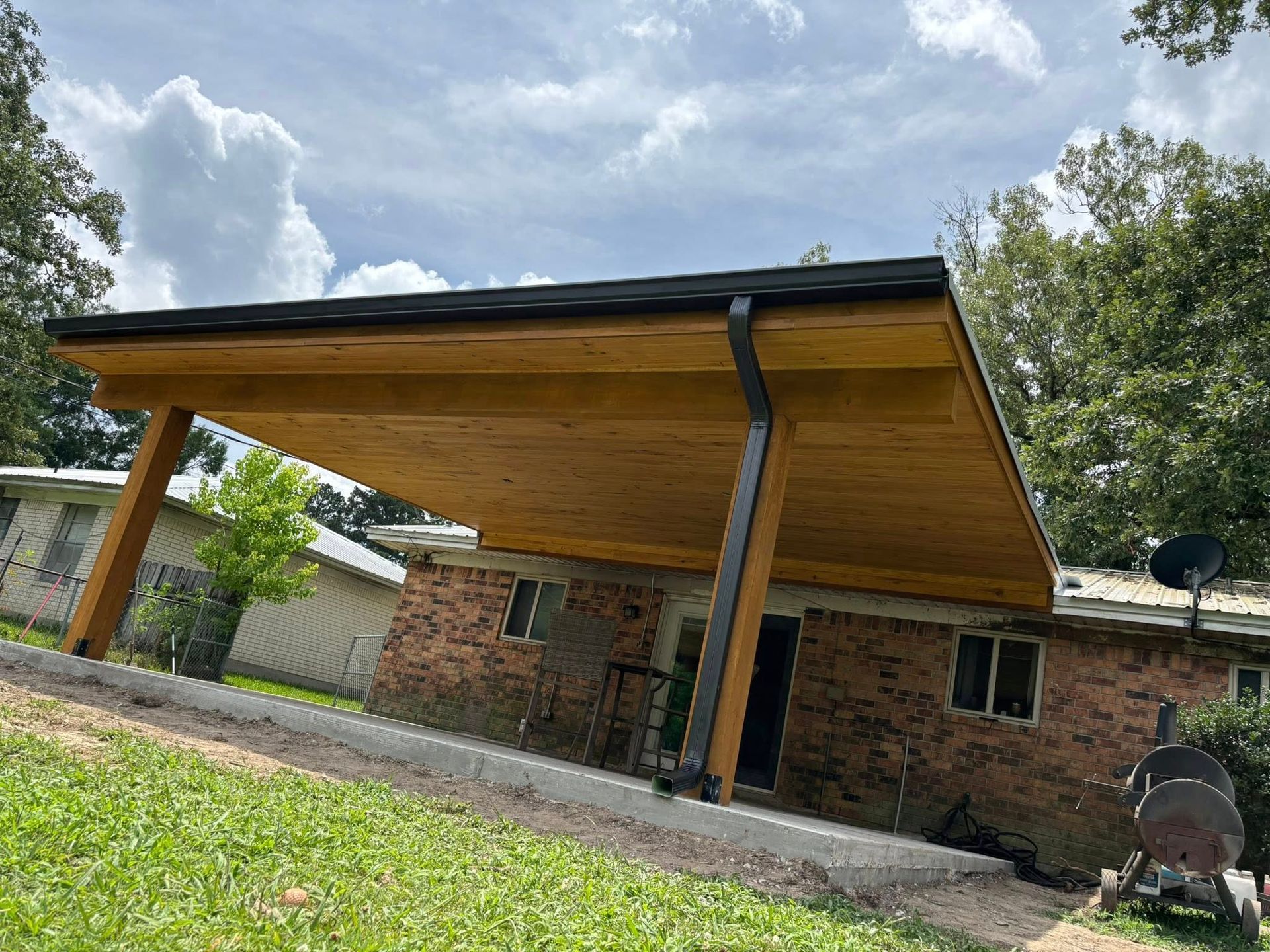 A wooden covered porch is sitting in front of a brick house.