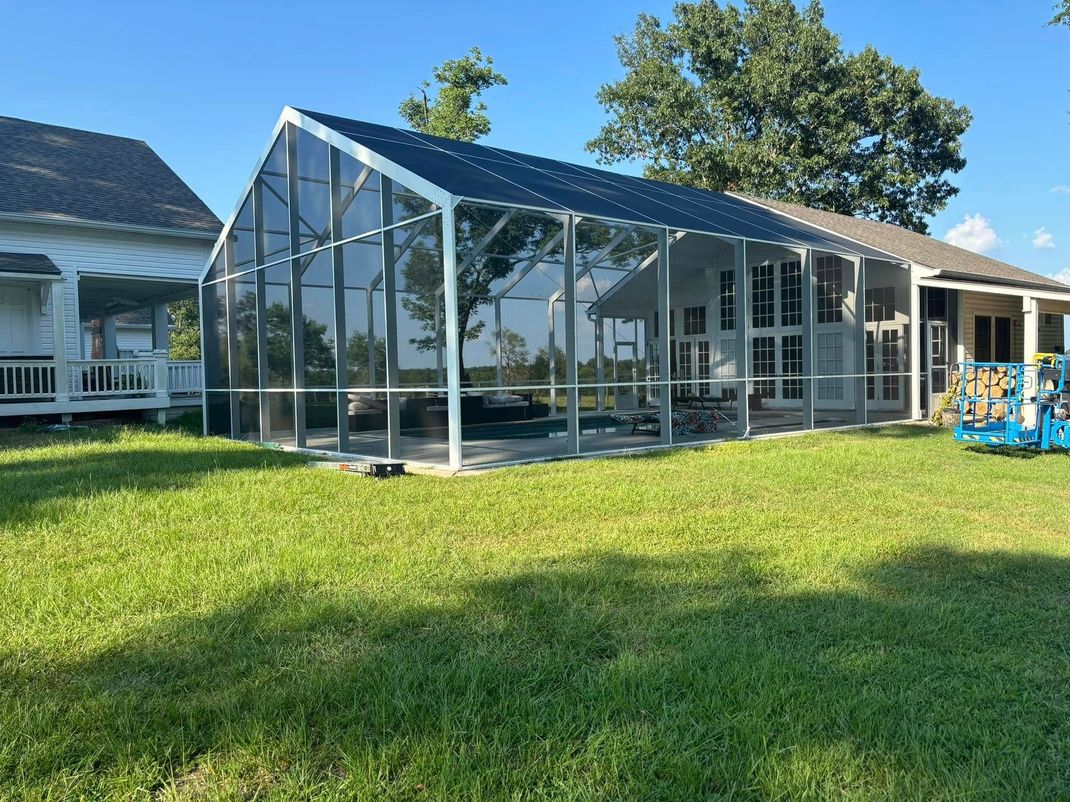 A large screened in porch is in the backyard of a house.