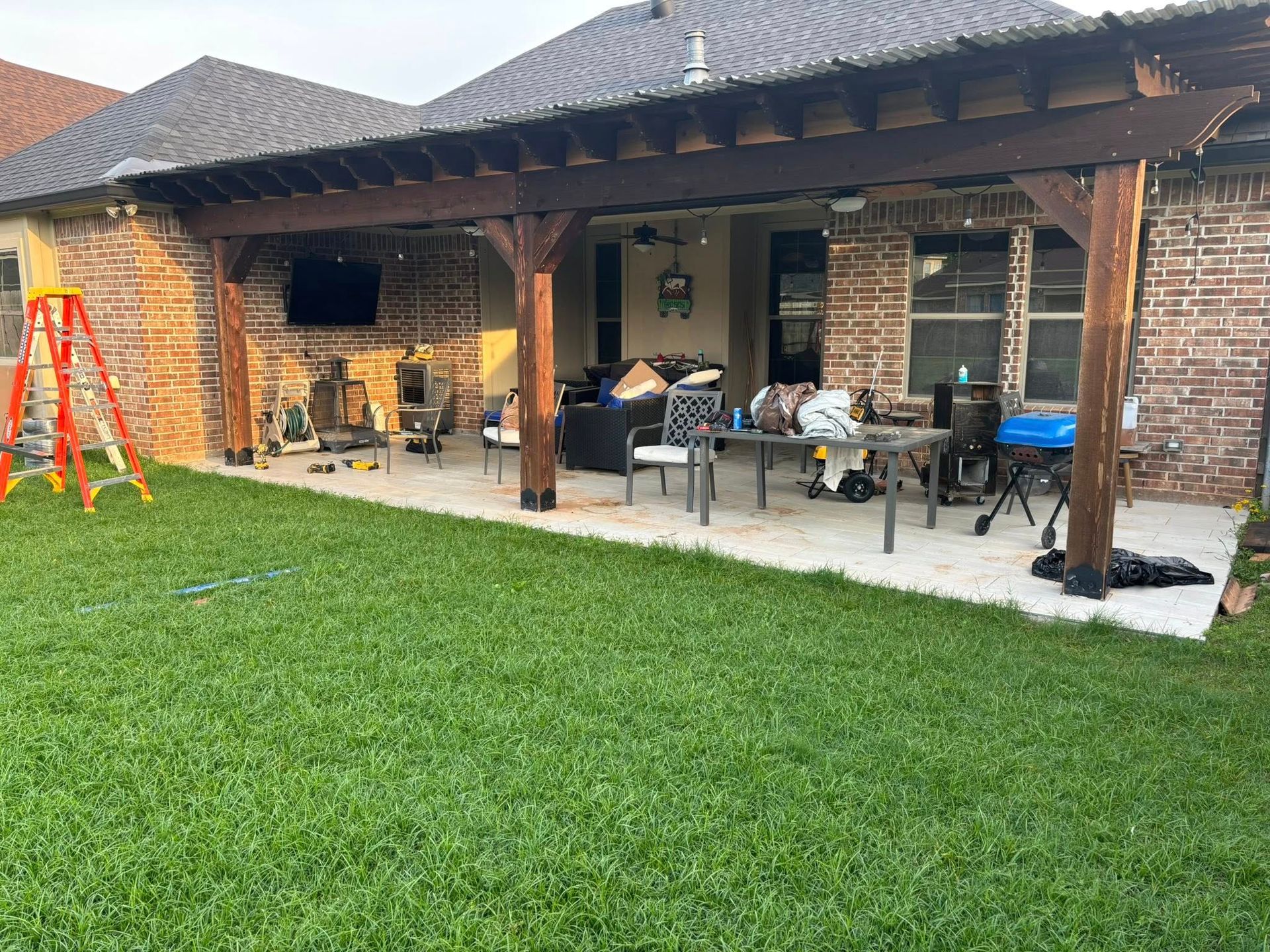 A patio with a wooden pergola and a ladder in the backyard of a house.
