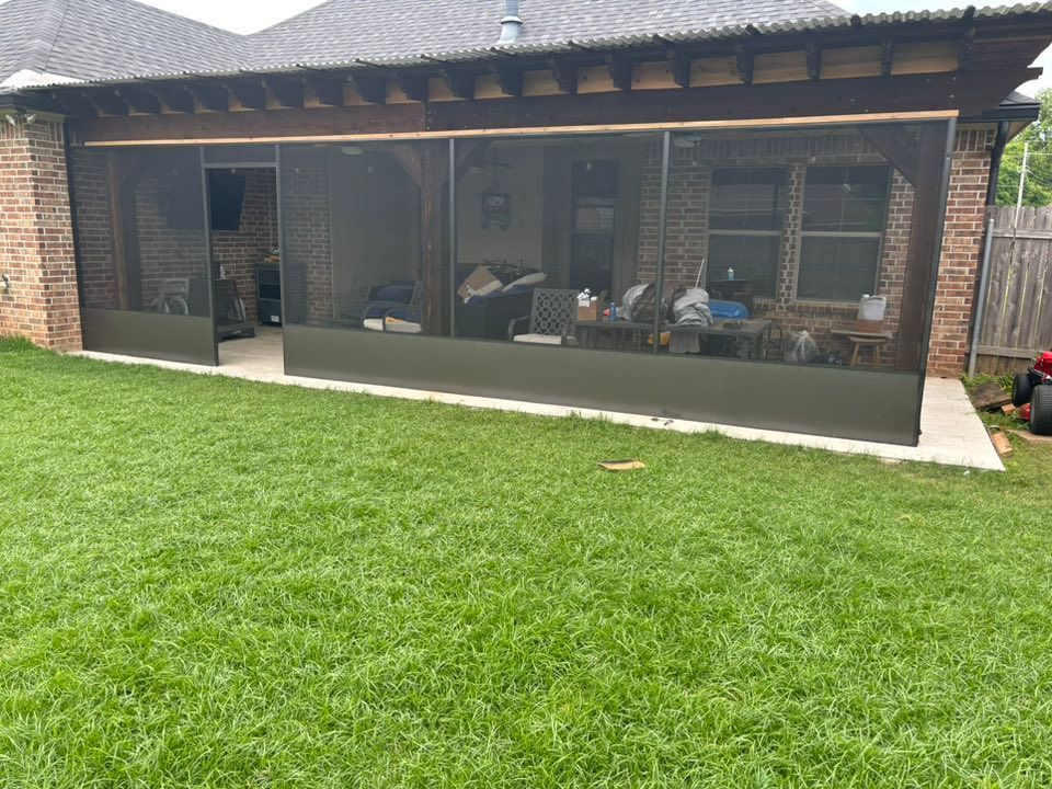 A screened in porch with a brick building and a lush green lawn in front of it.
