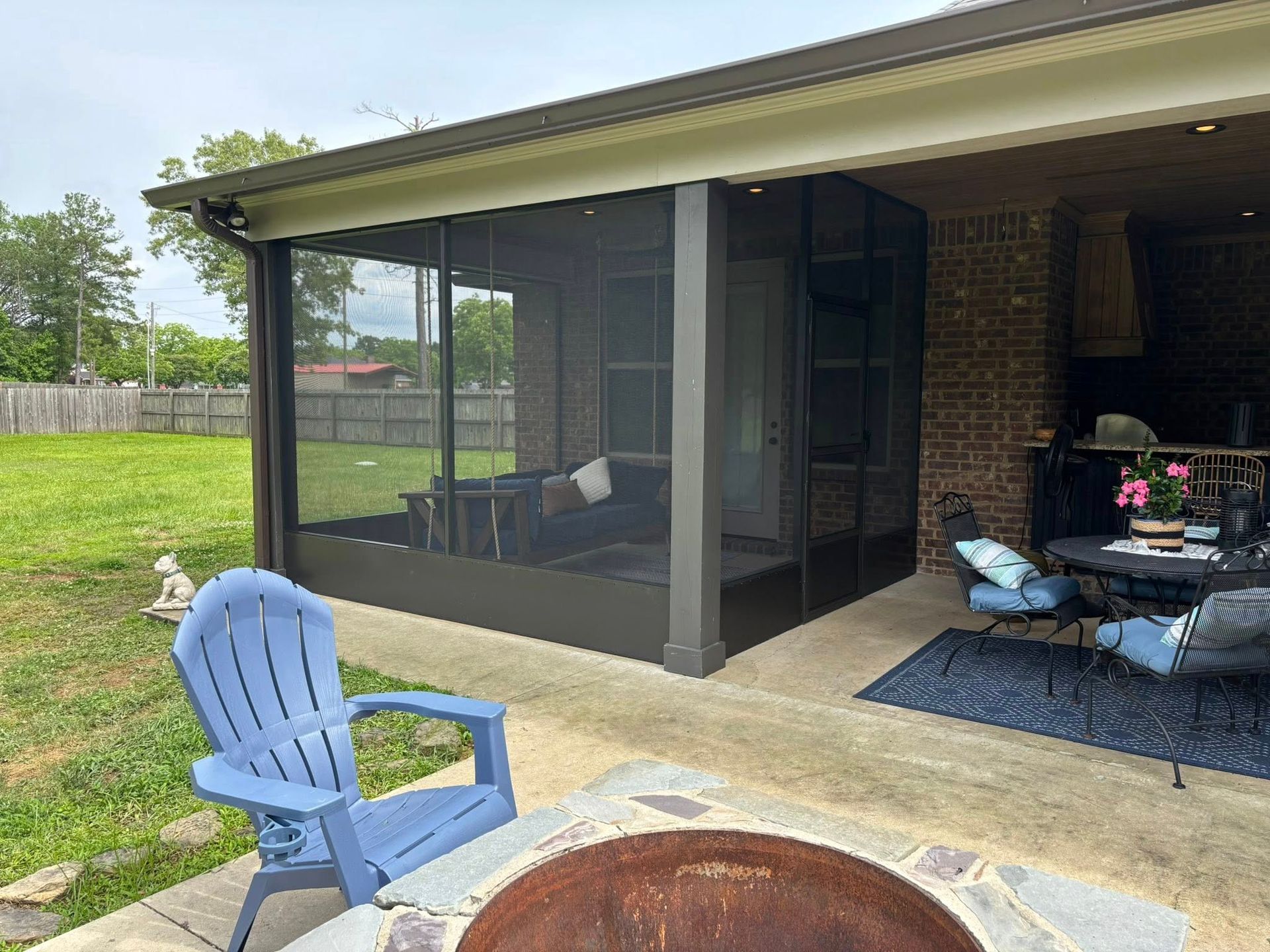 A screened in porch with a blue chair and a fire pit.