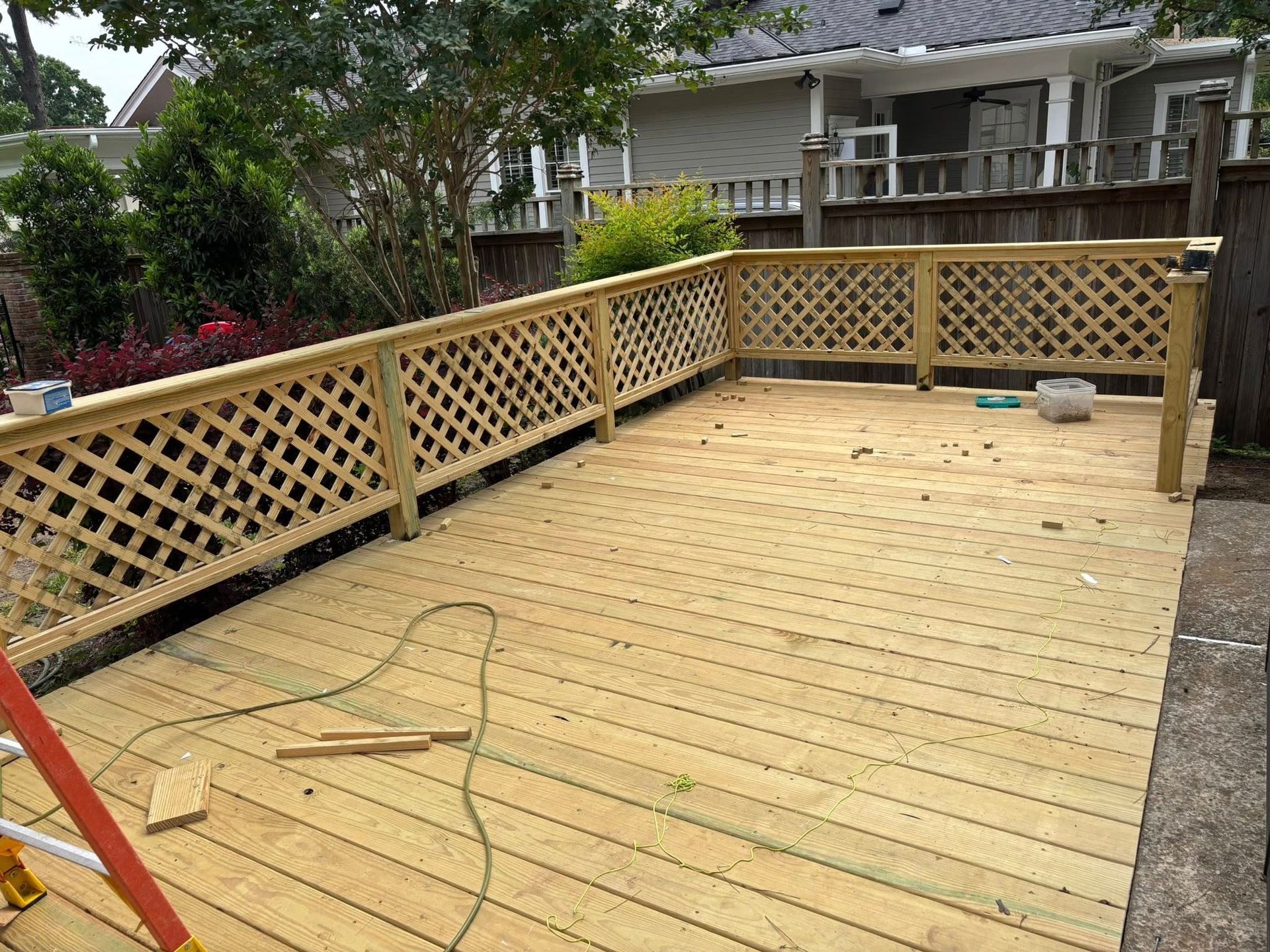 A wooden deck with a lattice railing is being built in a backyard.