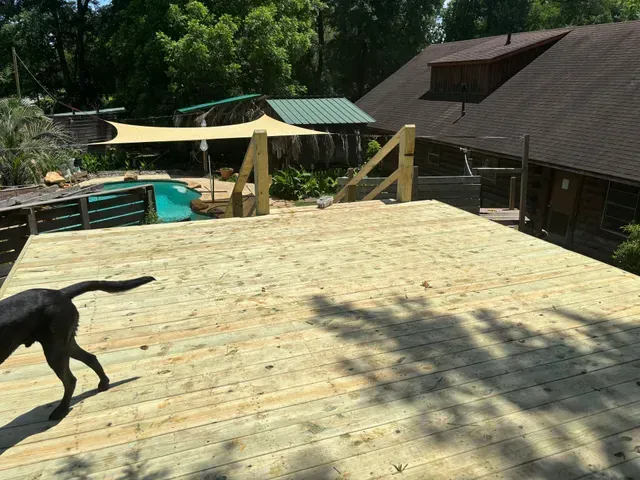 Wooden deck overlooking a pool and shaded yard, with a black dog at the left edge.