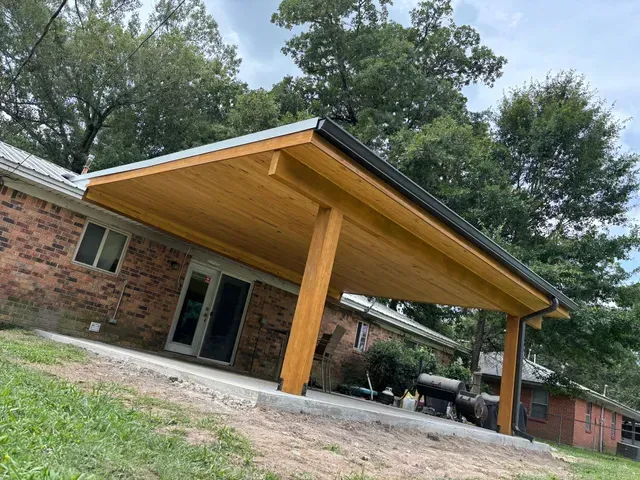 Brick house with a large wooden carport and slanted roof, set under trees