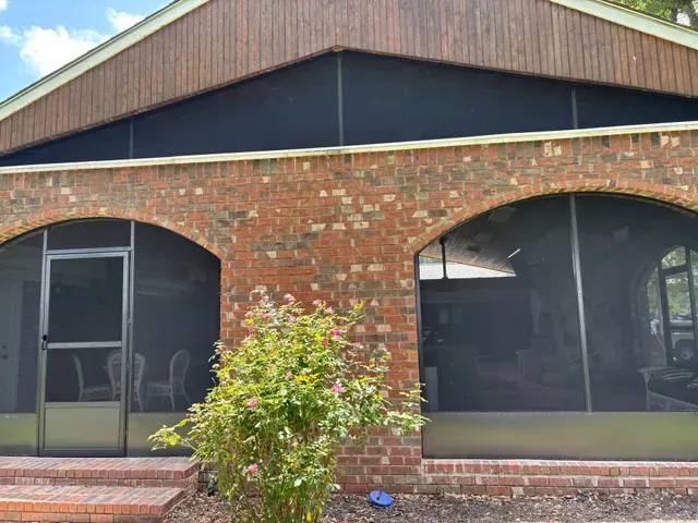 Brick house facade with arched windows, a central shrub, and a gabled roof.