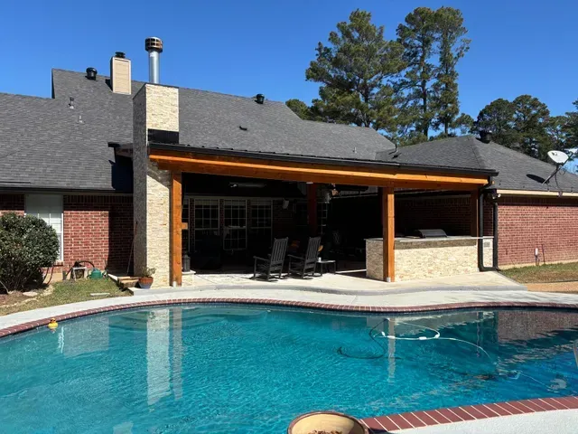 Backyard pool beside a brick house with a covered patio and blue sky
