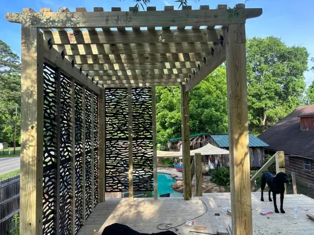 Wooden pergola with lattice walls overlooking a backyard pool and patio, with a black dog nearby