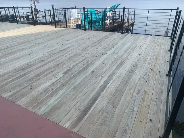 Wooden rooftop deck with black railing, turquoise chairs, and a red mat on the left