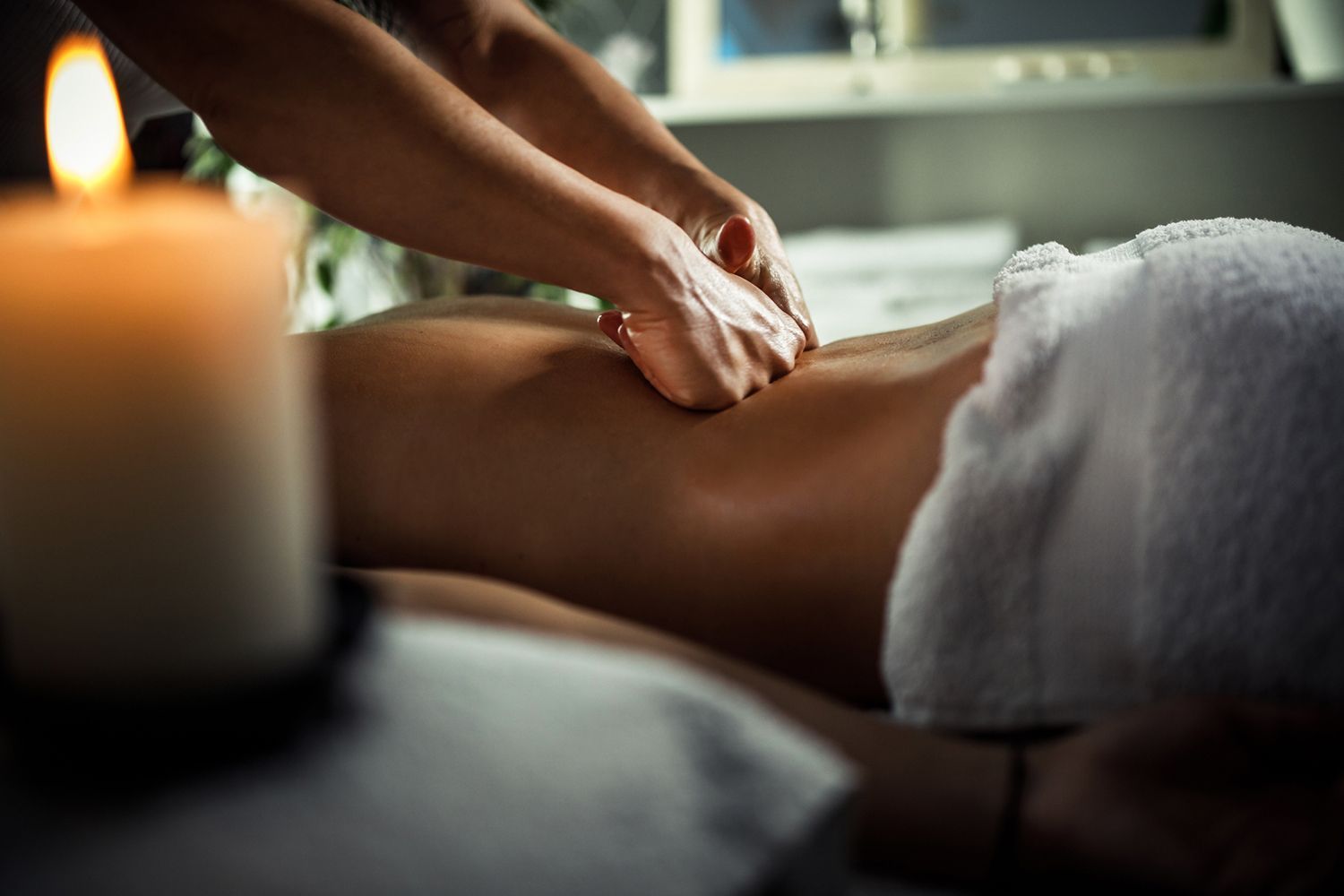 Person receiving a back massage at a spa with a lit candle nearby.