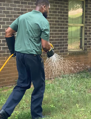 A man is watering a lawn with a hose in front of a brick building.