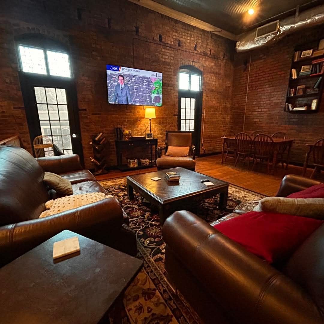 A cozy living area featuring leather couches, a wooden coffee table, and a TV on an exposed brick wall.