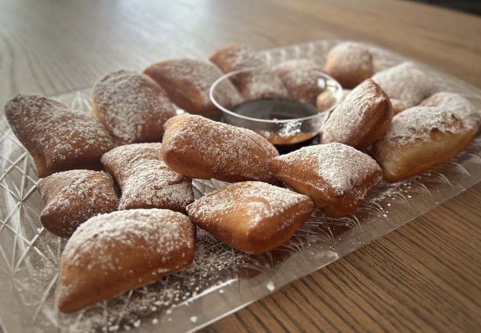 A tray of donuts with powdered sugar and syrup on a wooden table.