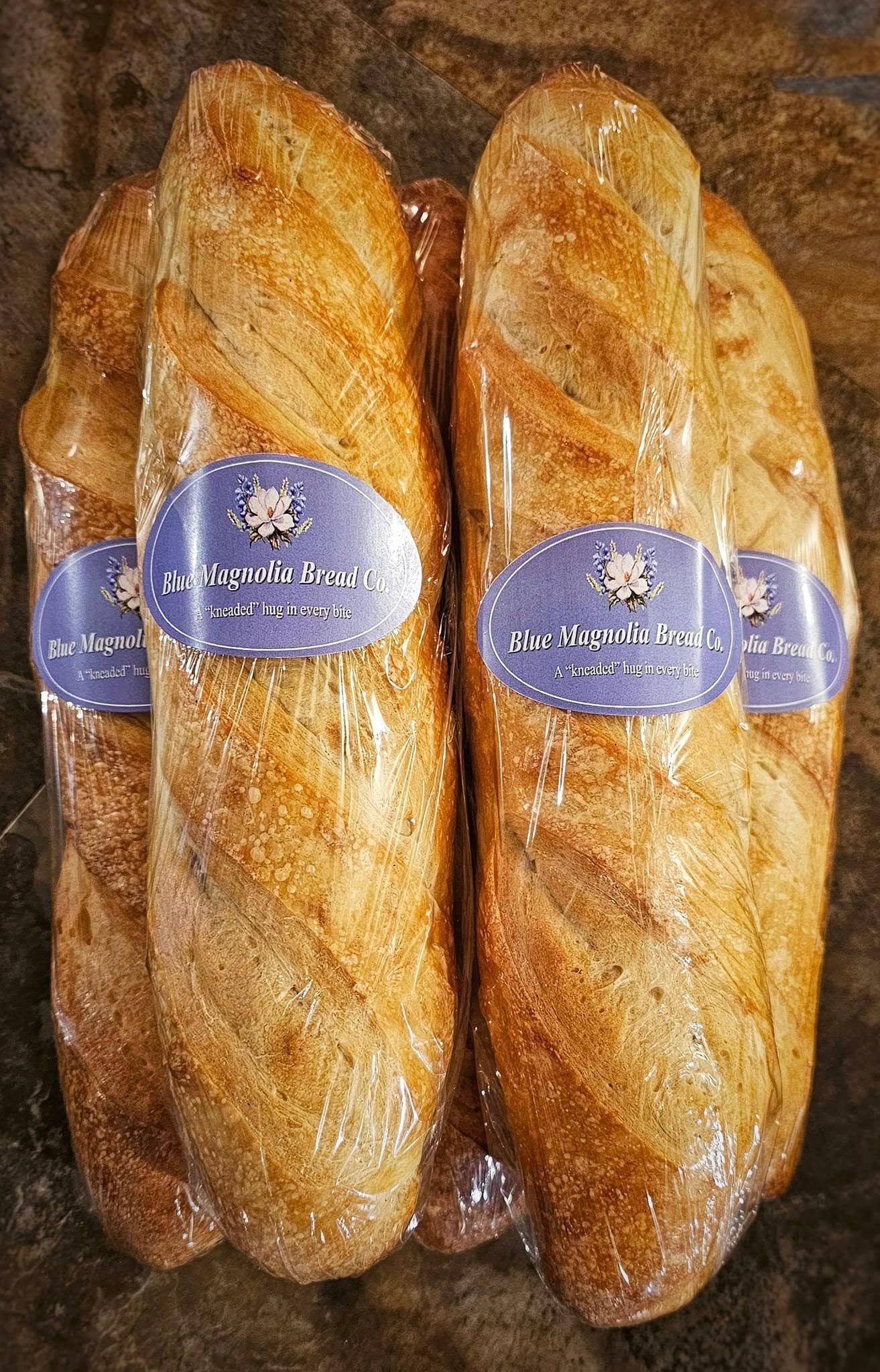 Two loaves of bread are wrapped in plastic and sitting on a table.