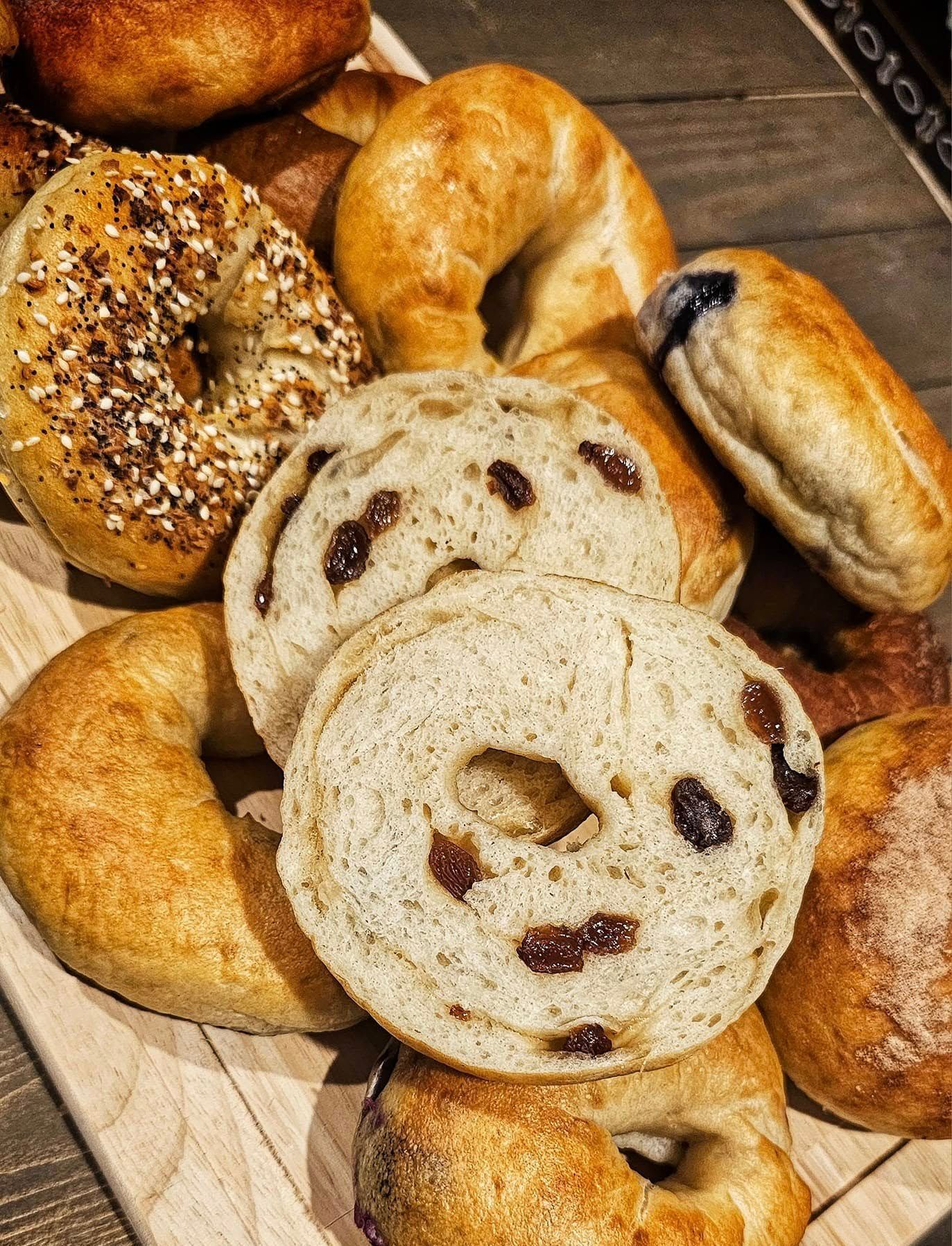 A variety of bagels are stacked on top of each other on a wooden cutting board.