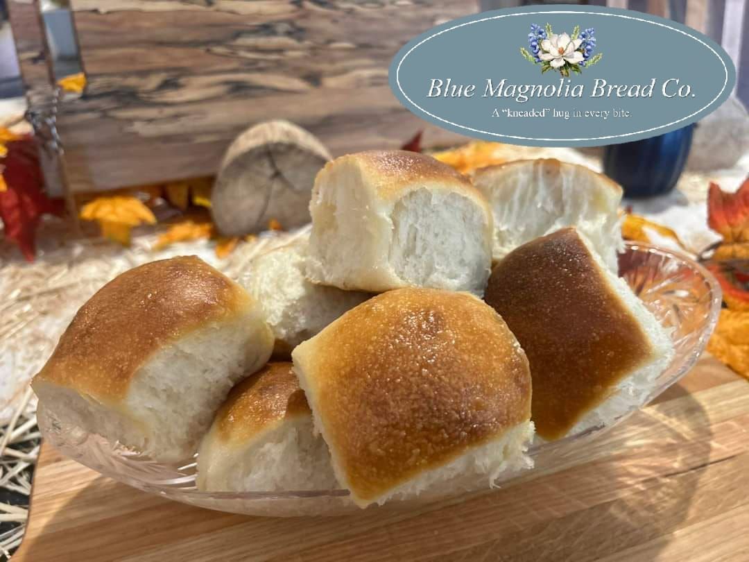 A glass bowl filled with rolls is sitting on a wooden table.