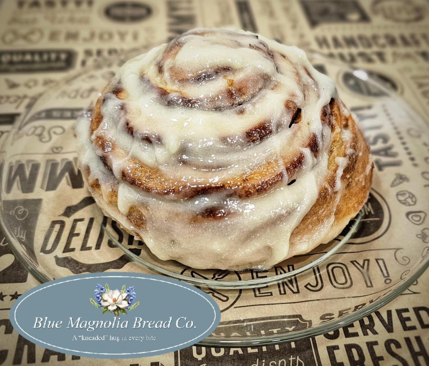 A cinnamon roll is sitting on a glass plate on a table.