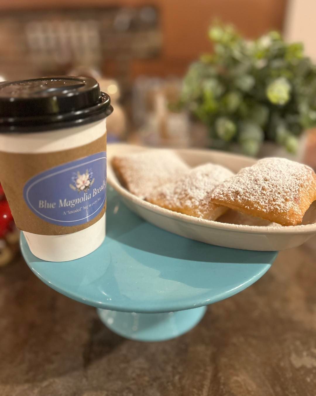 A cup of coffee and a plate of powdered sugar pastries on a cake stand.