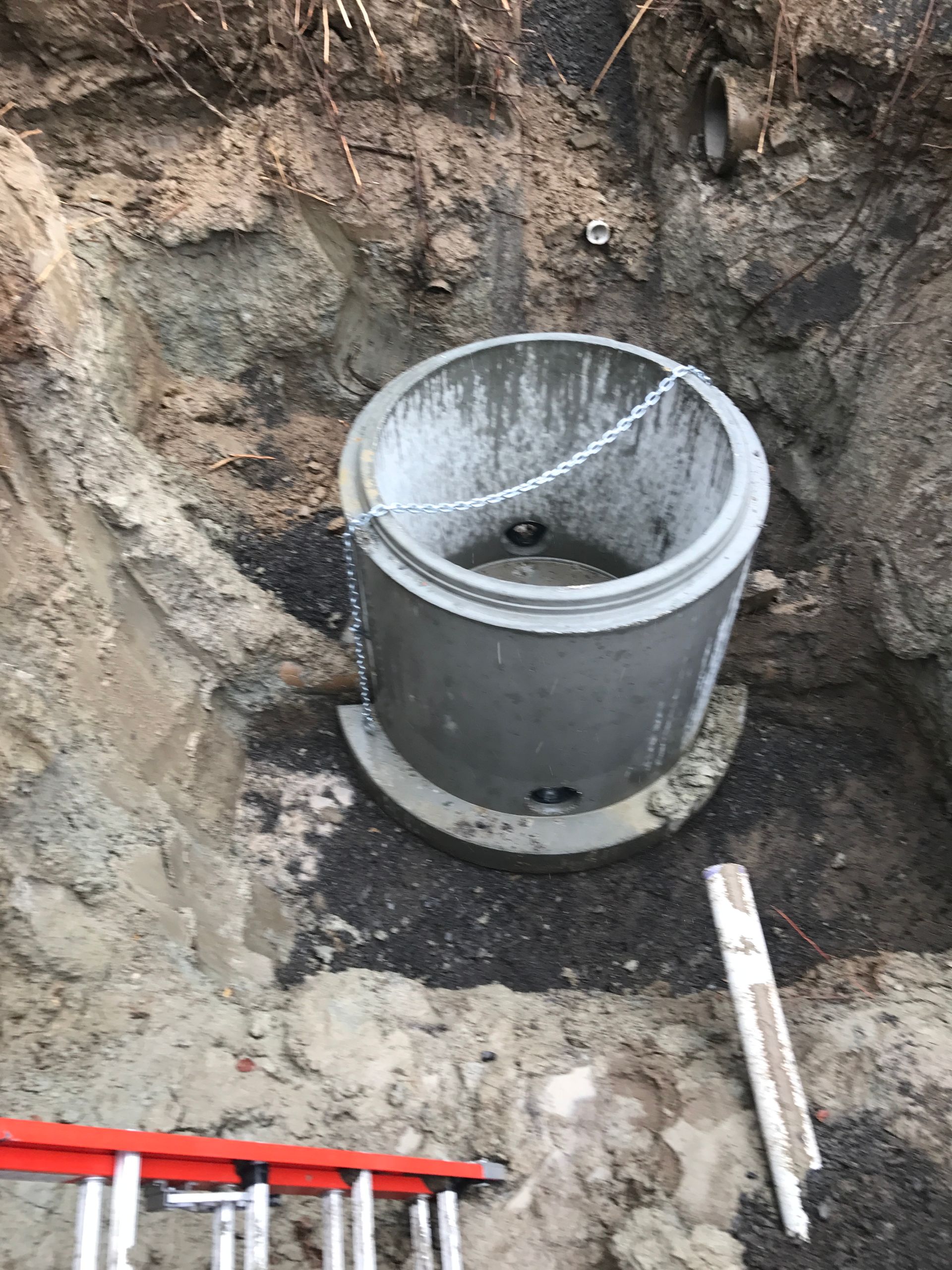 A large concrete ring is sitting in the dirt next to a ladder.