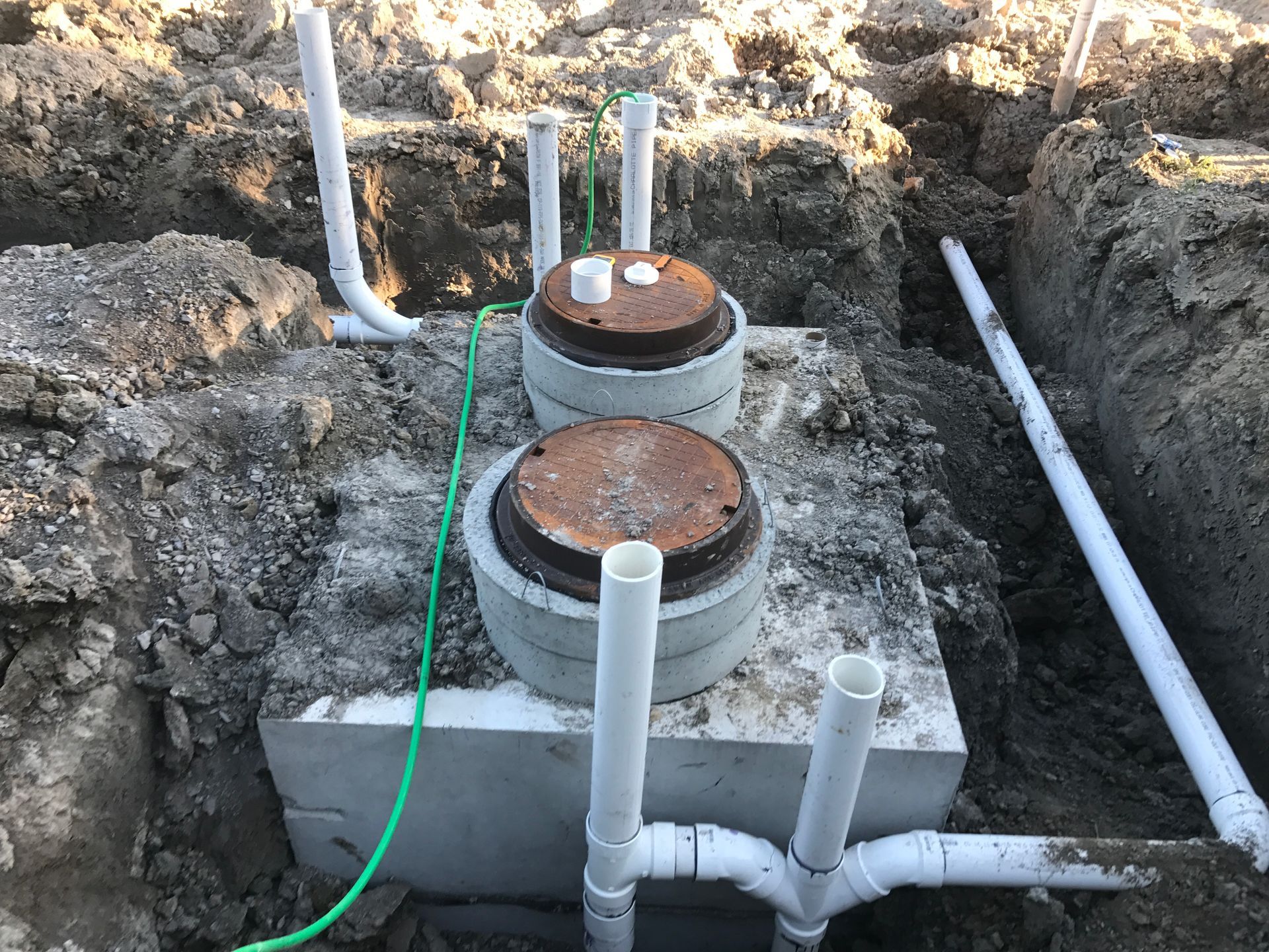 A septic tank is being built in the dirt with a green hose attached to it.
