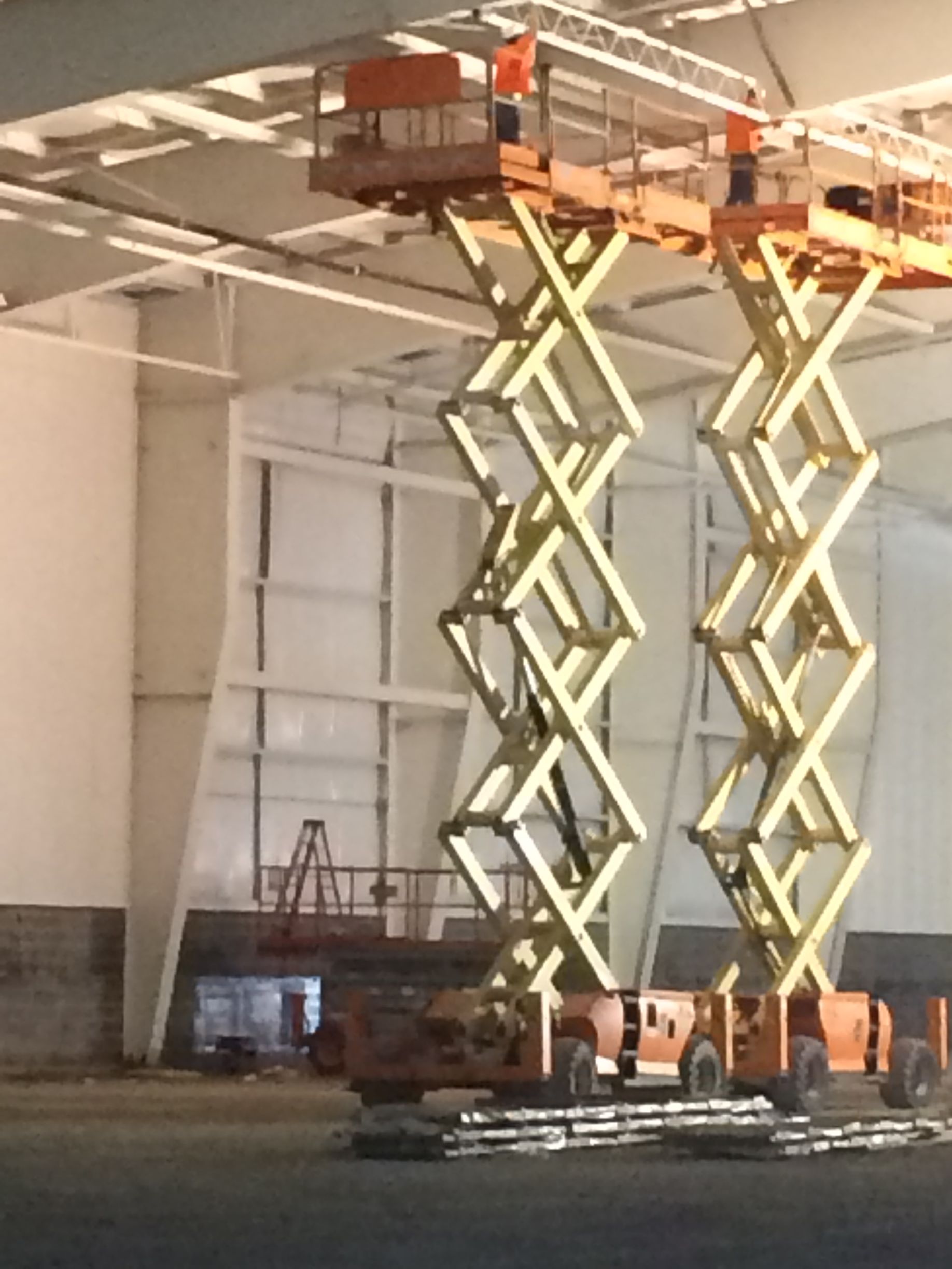 Two scissor lifts are in a large building
