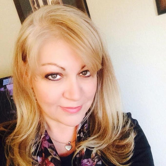 A woman with blonde hair is wearing a scarf and necklace