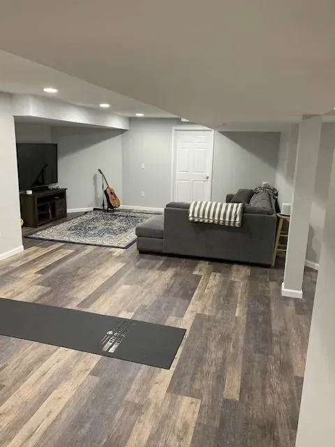 A living room in a basement with a couch and a yoga mat.