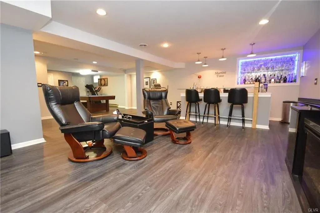 A basement with a bar , chairs , ottomans and a pool table.