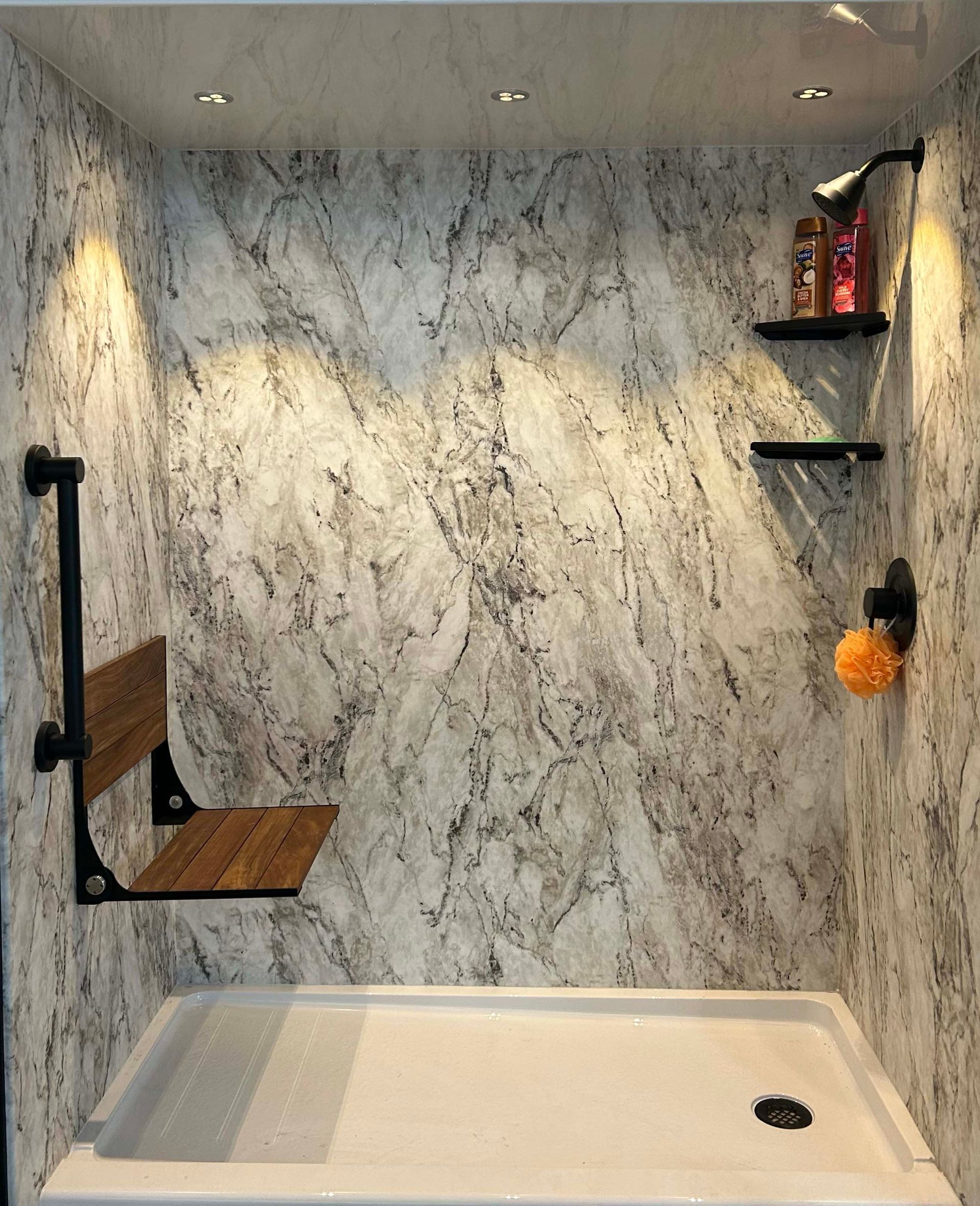 A bathroom with marble walls and a shower with a wooden seat