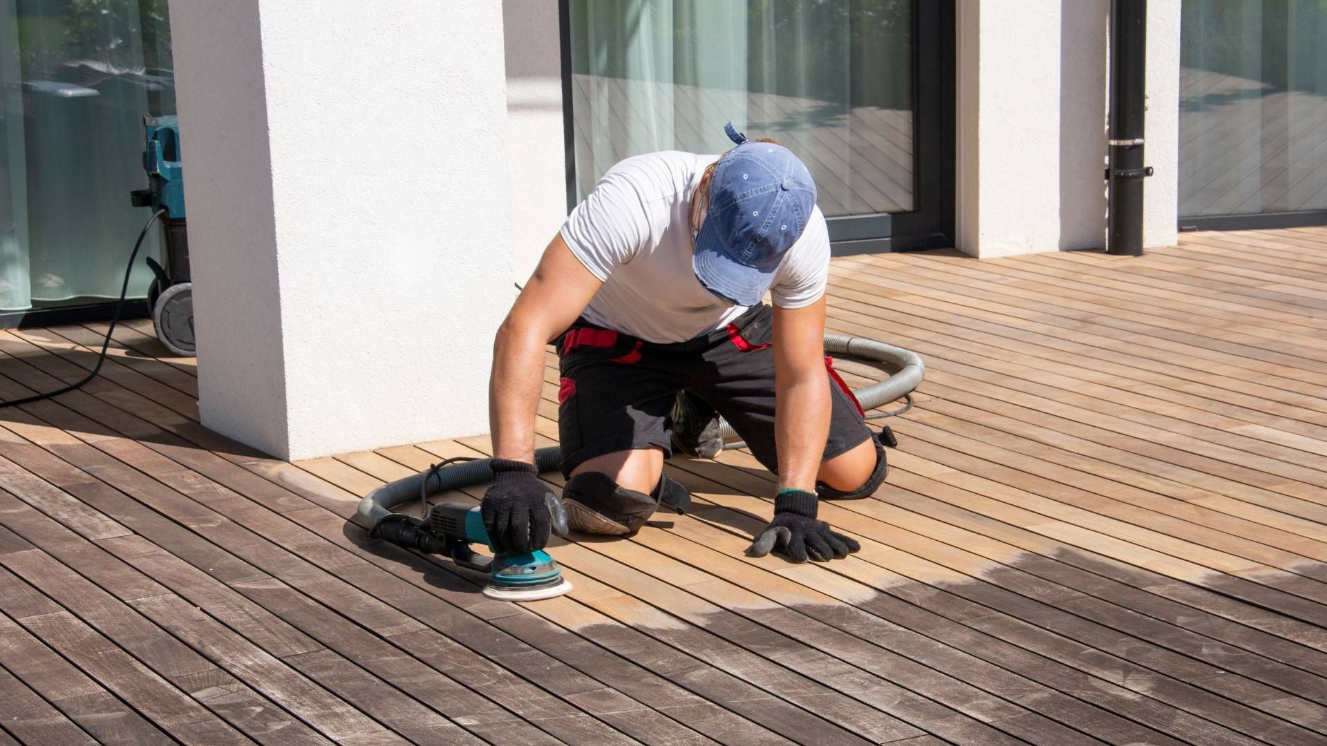 A man is sanding a wooden deck with a sander.